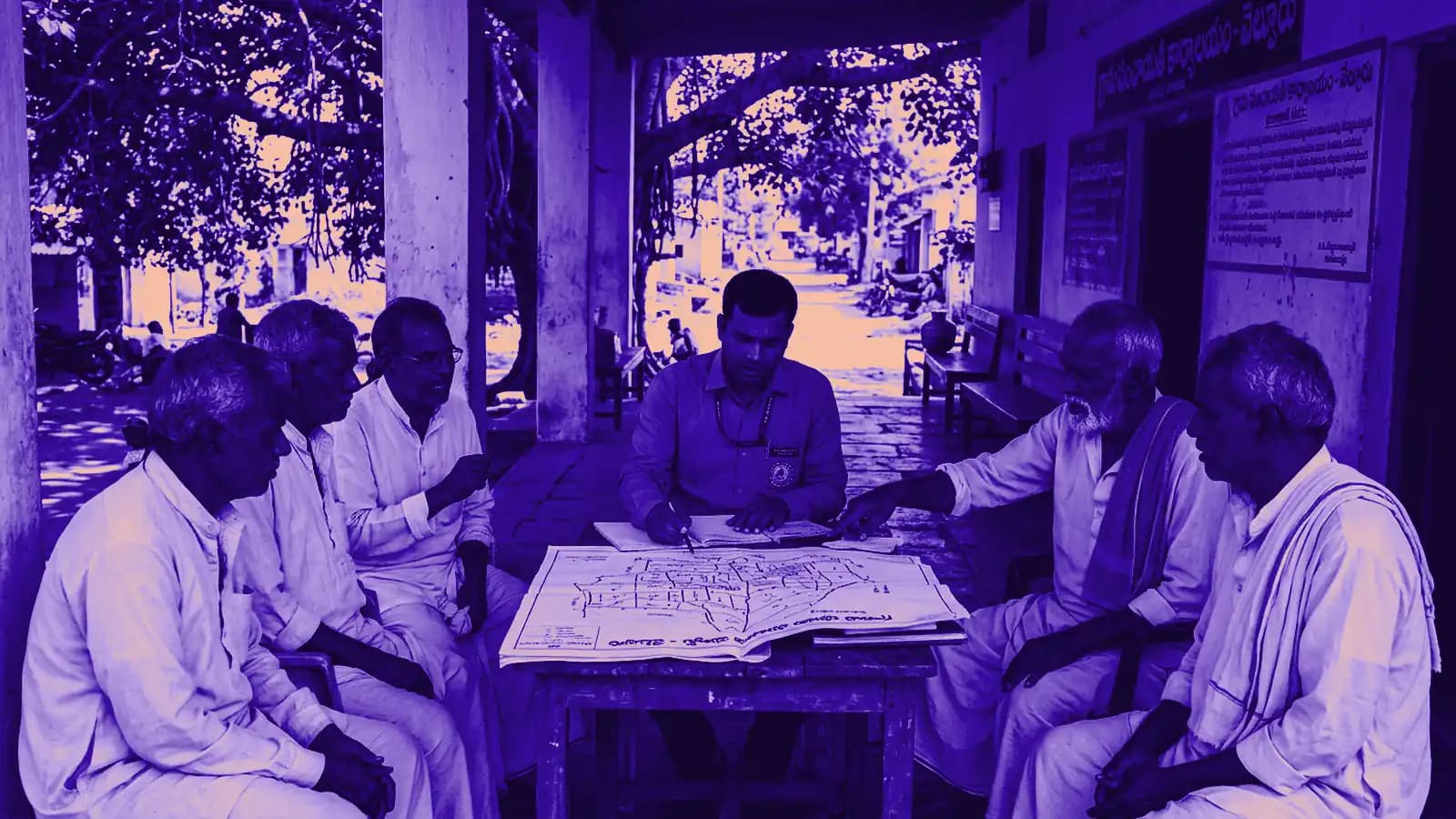 Gram Panchayat Secretary verifying land registry map with village elders on office porch under banyan tree shade